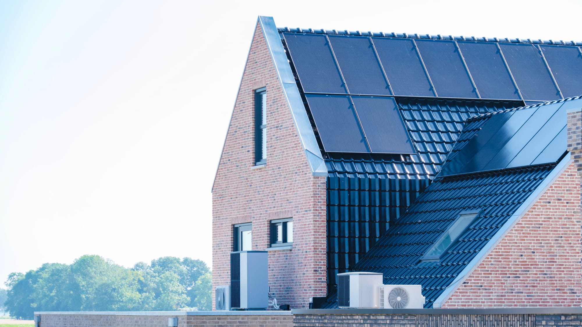 Brick house with a sloped roof covered in dark solar panels and outdoor HVAC units on the lower roof line; trees in the background
