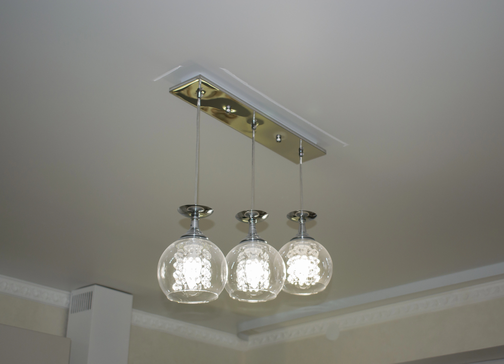 Three glass pendant lights with round shades hang from a metallic ceiling mount, accented by adjustable downlights.