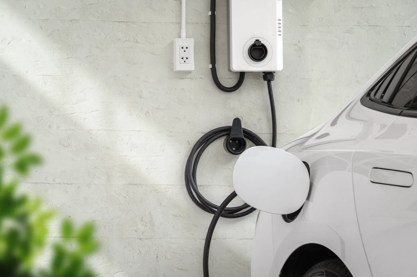 White electric car plugged into a wall charger, showing Home EV Charger Installation and modern charger options.