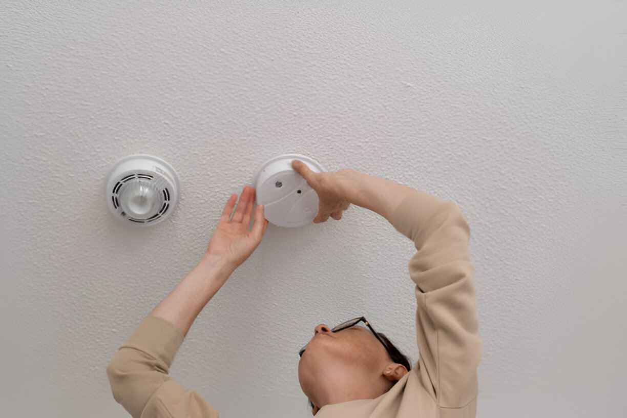 A person installs a smoke detector on a white ceiling near another device, showing pro smoke alarm installation in Eastern Suburbs.